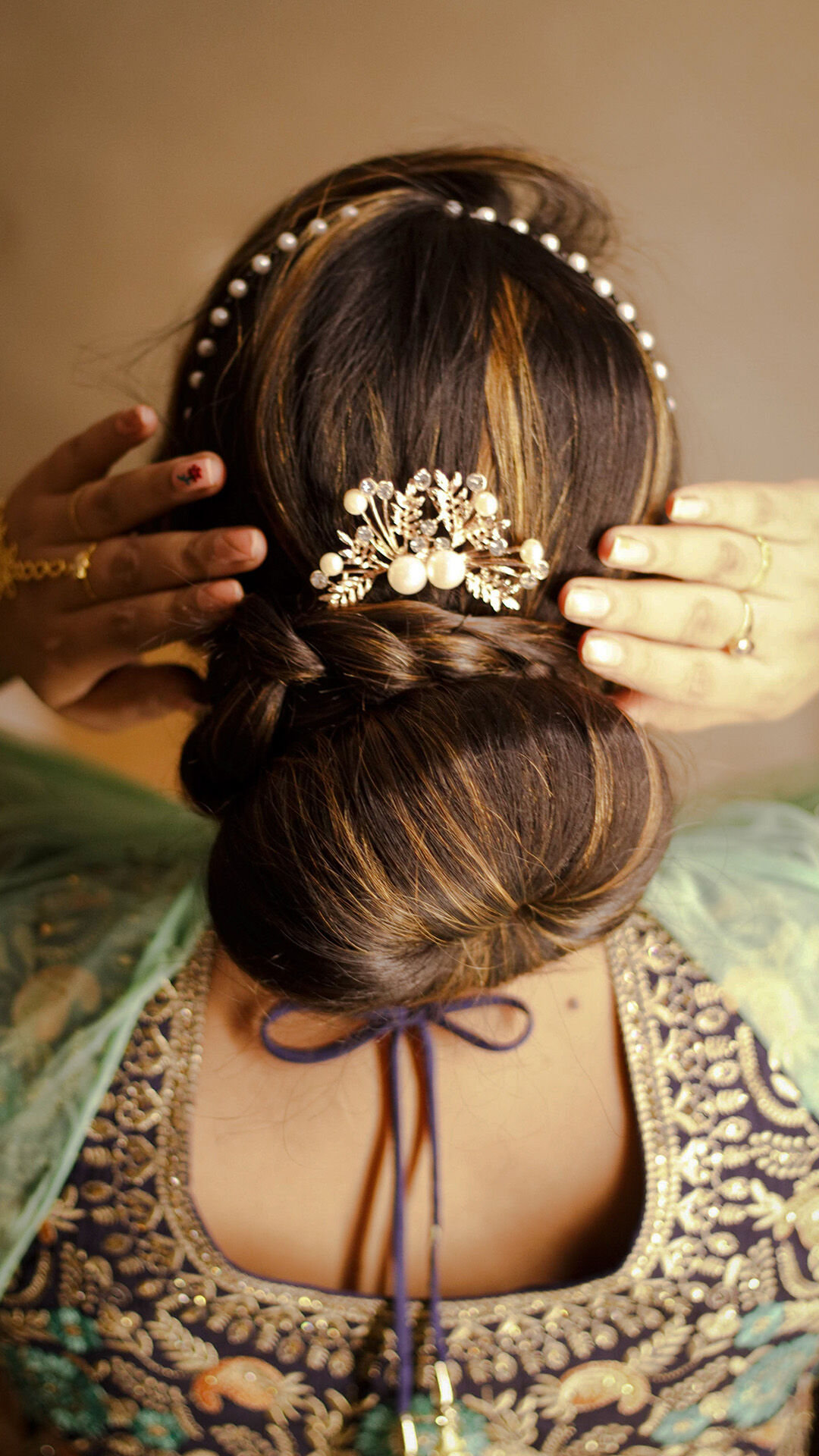 Close-up of a Gujarati bride’s low mogra-inspired bun with braided crown, pearl headband, and embellished floral hairpin — traditional bridal hairstyle with modern elegance.